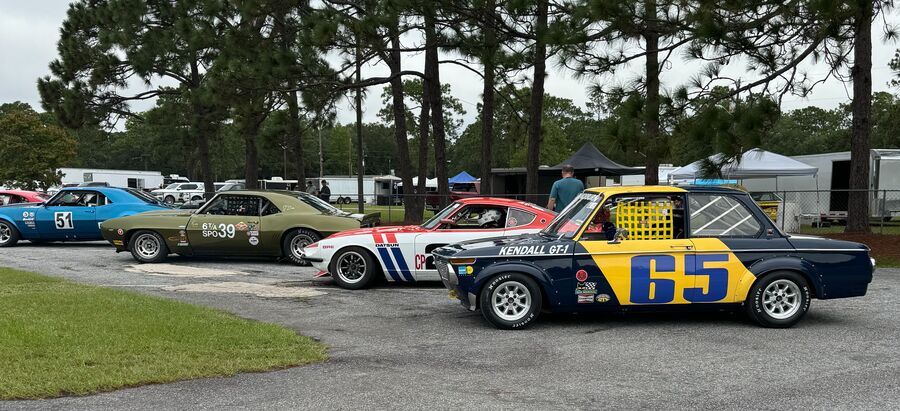 Navy and yellow BMW 2002 number 65 in the assembly area at Roebling Road, with a Camaro, a Datsun and a Mustang queued ahead