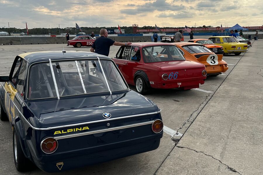 Rear view of a navy BMW 2002 at the head of a line of historic race cars on the pre-grid at Sebring